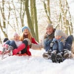 Family Having Fun Sledging Through Snowy Woodland