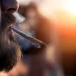 Man smoking marijuana cigarette outside on sunset